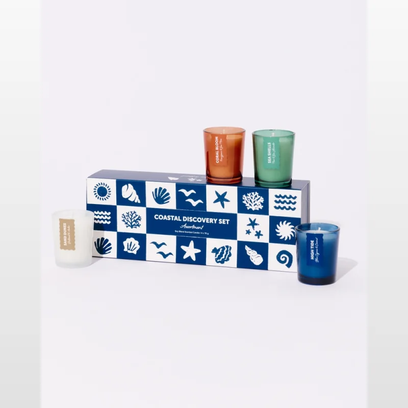 A set of four mini scented candles in glass jars, presented with a decorative box featuring coastal motifs. The candles are in amber, green, white, and blue glass jars.