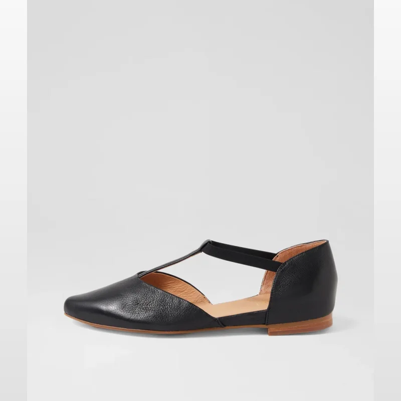 A black leather flat shoe with a t-bar strap and a pointed toe, shown from the side against a white background.