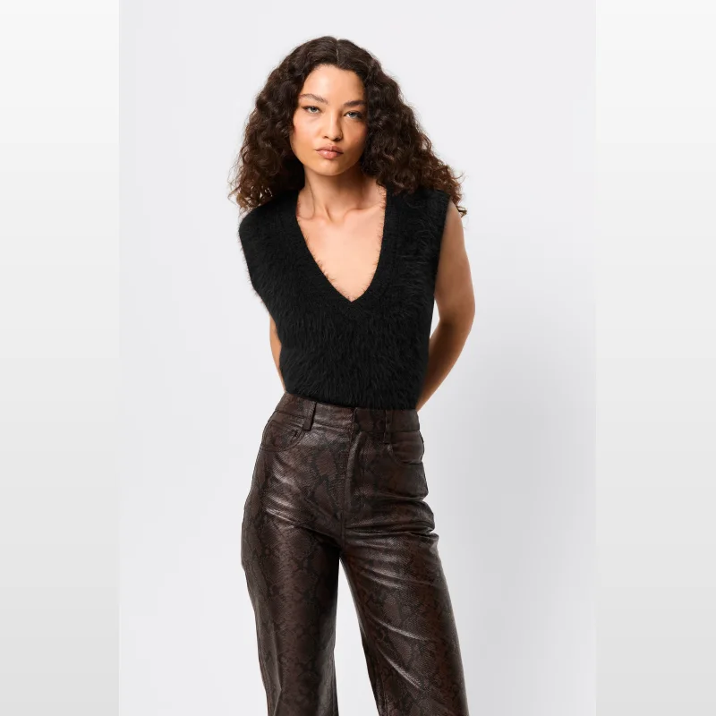 Woman wearing a black fuzzy V-neck sleeveless knit vest with brown snake-print trousers.