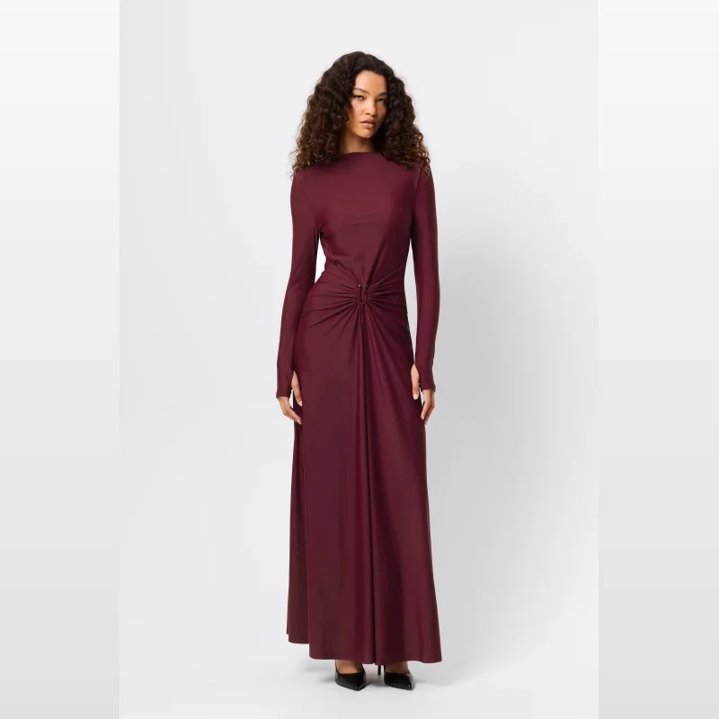 Woman wearing a long-sleeved, burgundy maxi dress with a draped waist and silver U-shaped detail.