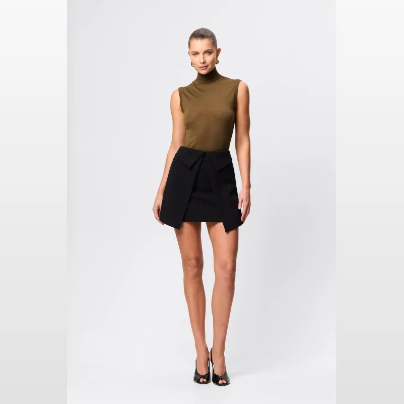 Woman wearing a black Mossman Even Odds Mini Skirt with a unique folded waistband detail and a green sleeveless turtleneck top.