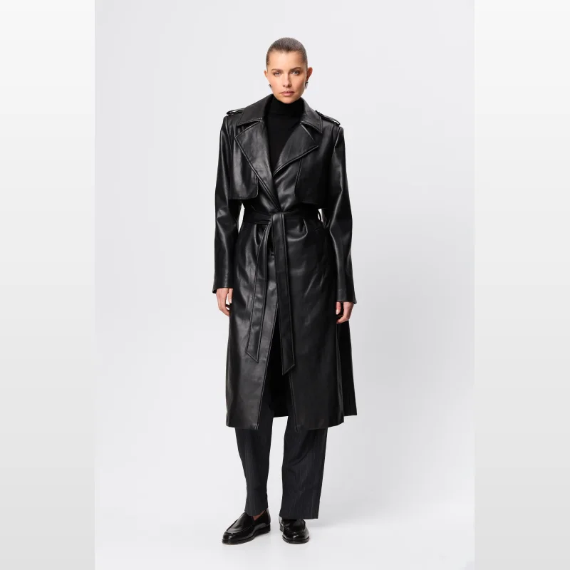 Woman wearing a black faux leather full-length trench coat with a belted waist and structured lapels.