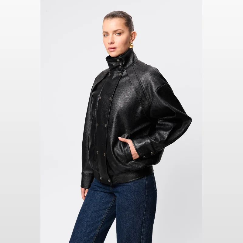 Woman wearing a black Mossman Jordan Jacket made of pebbled faux leather, featuring a funnel neck and press stud closure.