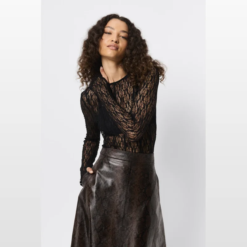 Woman wearing a black sheer lace long-sleeve top with a crew neckline and thumbhole cuffs, paired with a brown snakeskin print skirt.