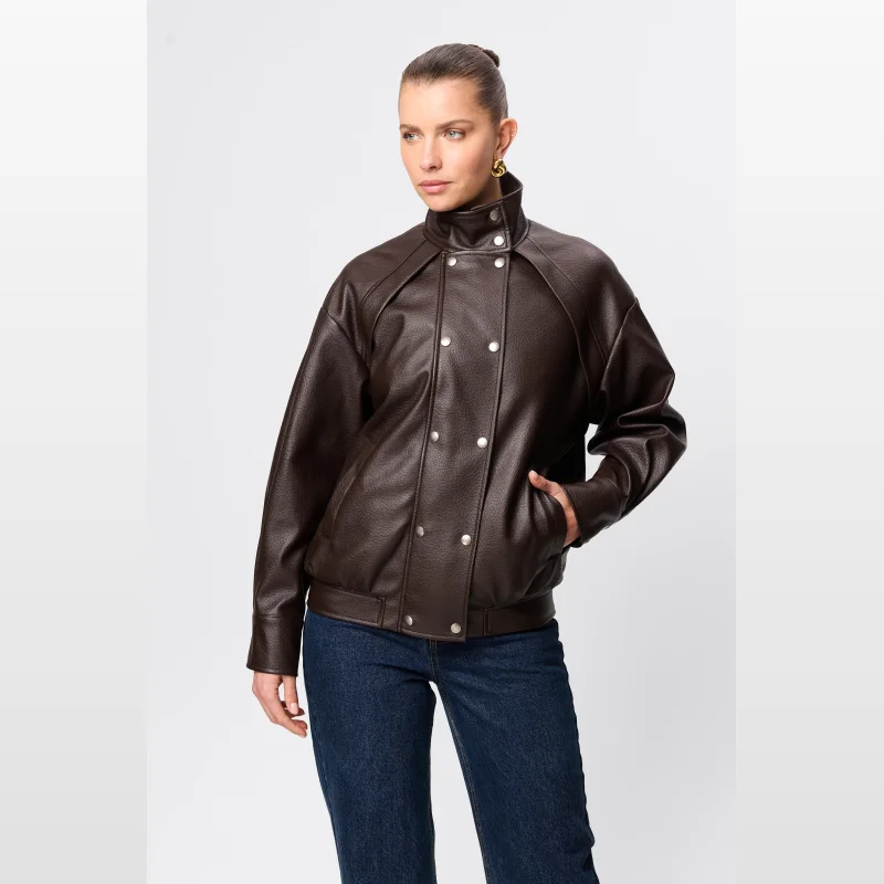 Woman wearing a brown pebbled faux leather Mossman Jordan jacket with a funnel neck and double press stud closure, paired with blue denim jeans.