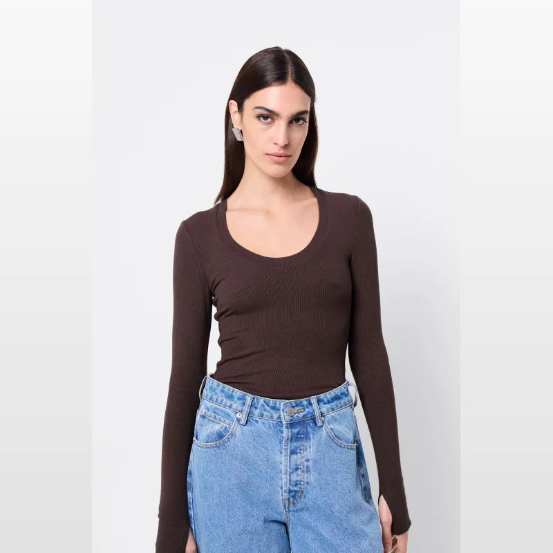 Woman wearing a brown ribbed long-sleeve top with a scoop neckline and thumbhole detail, paired with light blue denim jeans.