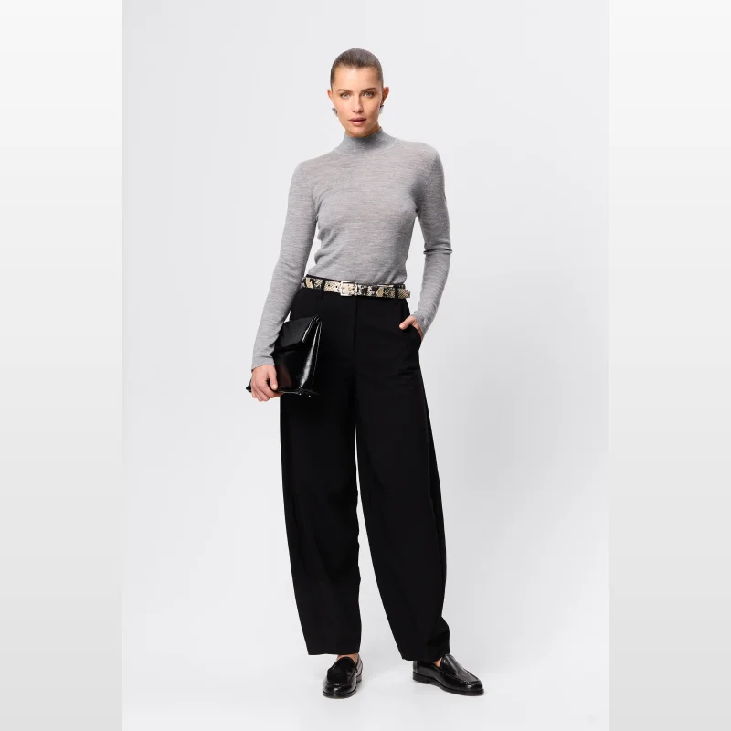 Model wearing Mossman Sonder Pant in black, a tailored, wide-leg trouser with a high waist, paired with a grey turtleneck, a snakeskin belt, and black loafers.