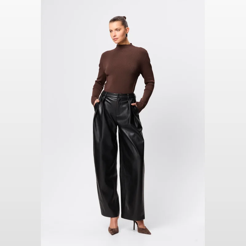 Model wearing Mossman Fairfax Pleated Wide Leg Trousers in black faux leather, styled with a brown ribbed turtleneck and brown pointed heels.